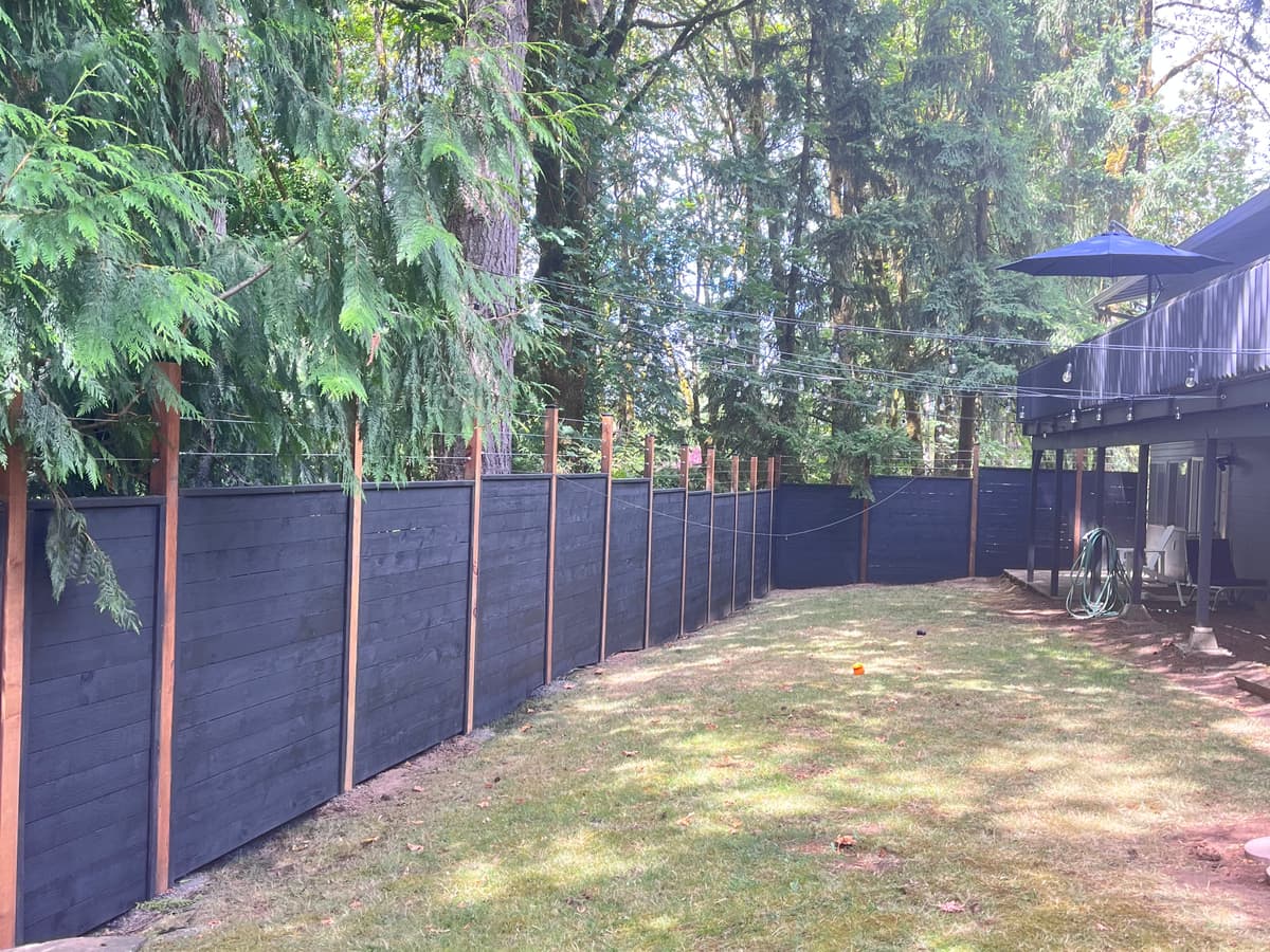 Black 8 ft privacy fence running the boundary of a wooded yard, by Handy Brothers LLC